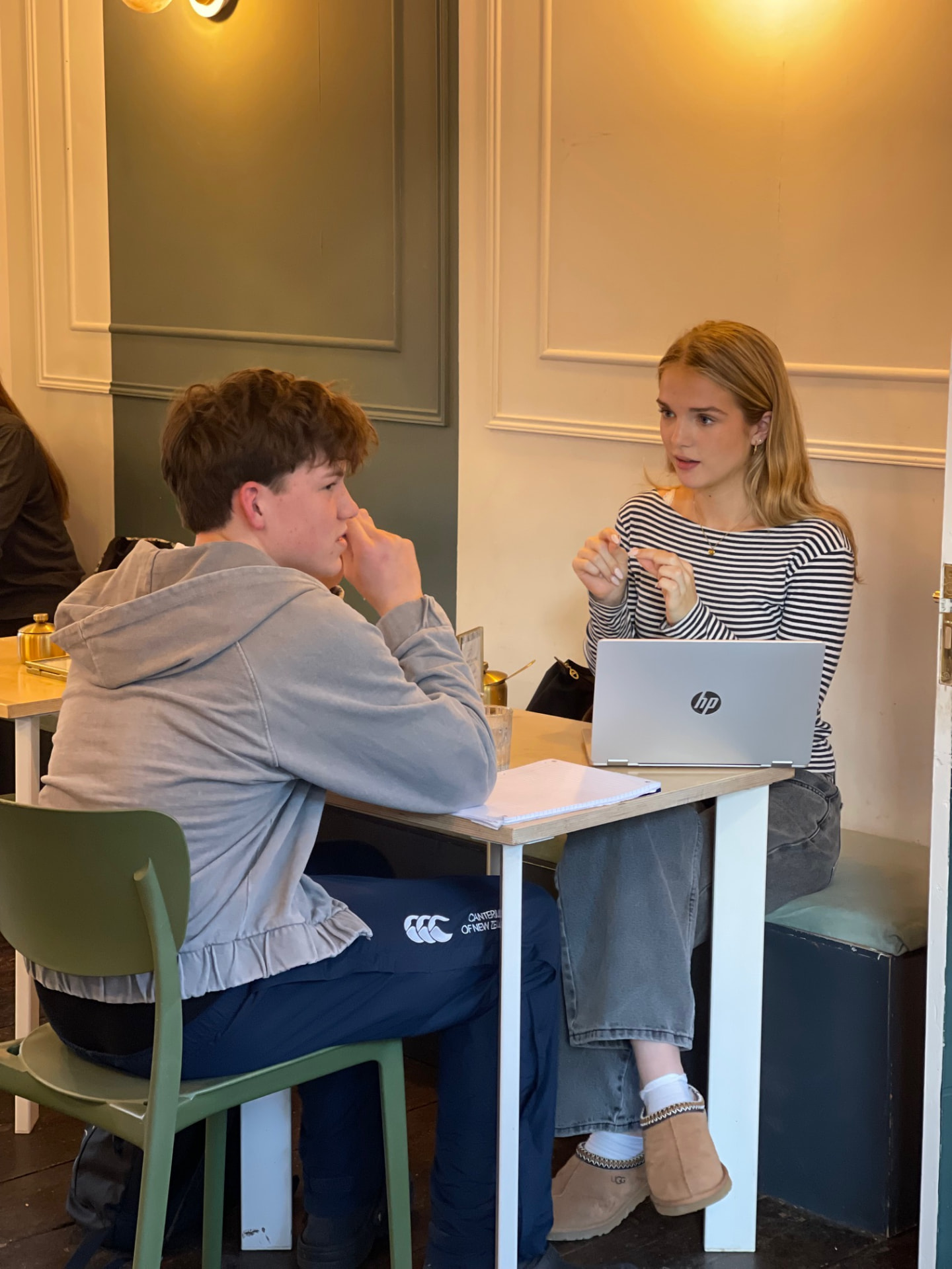 Two students talking across a table with a laptop